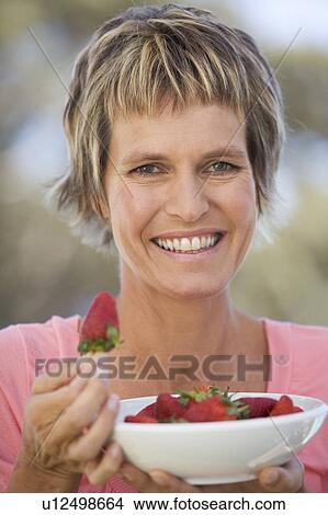 Picture - A woman eating a bowl of strawberries. Fotosearch