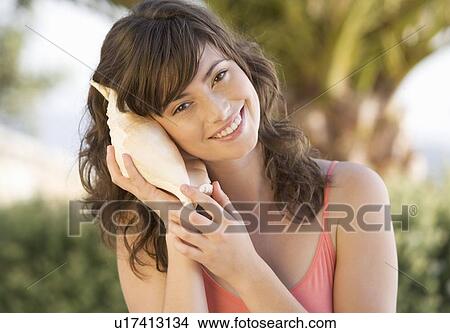 A woman holding a shell to her ear View Large Photo Image Picture - A woman holding a shell to her ear. Fotosearch