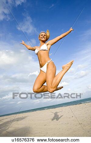 Stock Photograph - A woman in a bikini jumping on a beach. Fotosearch