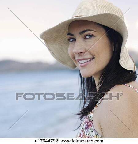 Stock Image - A woman in a hat standing on a beach. Fotosearch