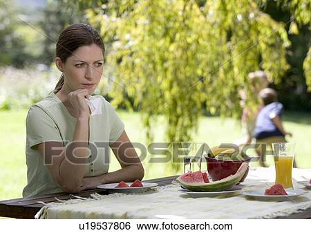 Stock Photograph - A woman looking sad and pensive sitting in the garden. Fotosearch