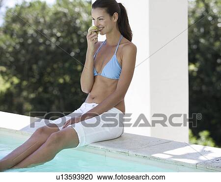 A woman sitting on the edge of a swimming pool eating an apple View Large Photo Image Stock Image - A woman sitting on the edge of a swimming pool eating an apple. Fotosearch