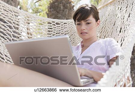 A woman using a laptop lying in a hammock View Large Photo Image Stock Photograph - A woman using a laptop lying in a hammock. Fotosearch