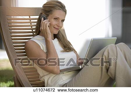 Stock Image - A woman using a mobile phone and laptop. Fotosearch