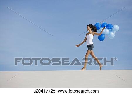 Stock Photography - A woman walking in the desert holding a bunch of balloons. Fotosearch