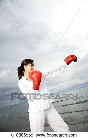 Stock Photography - A woman wearing boxing gloves on a beach. Fotosearch