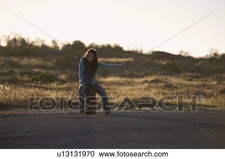 Stock Image - A woman with a suitcase hitching a lift. Fotosearch
