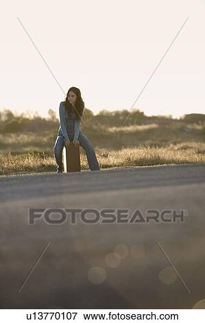 Stock Photo - A woman with a suitcase hitching a lift. Fotosearch