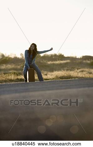 Stock Photography - A woman with a suitcase hitching a lift. Fotosearch