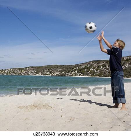 Stock Image - A young boy playing with a football on a beach. Fotosearch