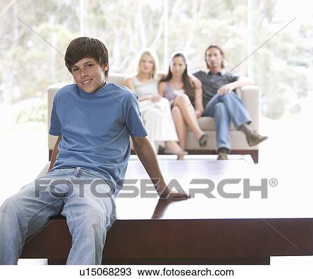 Stock Image - A young boy sitting on a coffee table with his family on the sofa. Fotosearch