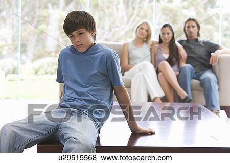 A young boy sitting on a coffee table with his family on the sofa View Large Photo Image Stock Photo - A young boy sitting on a coffee table with his family on the sofa. Fotosearch