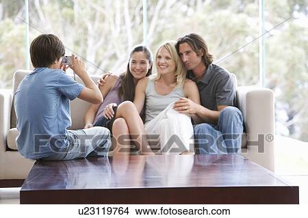 Picture - A young boy taking a photo of his family sitting on a sofa. Fotosearch