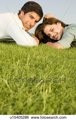 Stock Photograph - A young couple laying on grass. Fotosearch