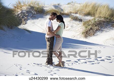 Stock Photo - A young couple walking in sand dunes. Fotosearch