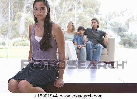 A young girl sitting on a coffee table with her family on the sofa View Large Photo Image Picture - A young girl sitting on a coffee table with her family on the sofa. Fotosearch