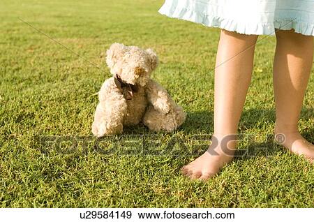Stock Photo - A young girl standing by a teddy bear. Fotosearch