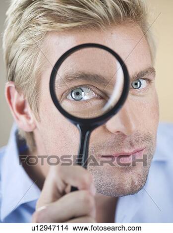 Picture - A young man looking through a magnifying glass. Fotosearch