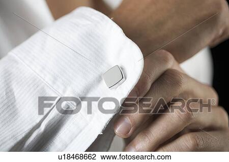 Stock Image - A young man putting on cufflinks, close-up. Fotosearch