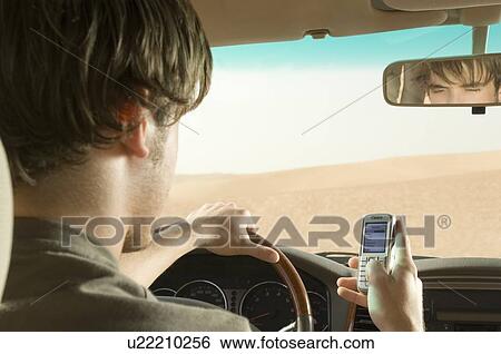 Stock Photograph - A young man using a mobile phone whilst driving. Fotosearch