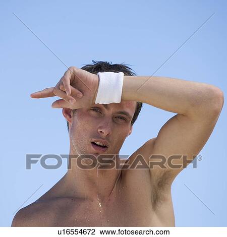 Stock Image - A young man wiping sweat from his face. Fotosearch