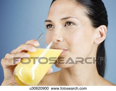 Stock Image - A young woman drinking a glass of orange juice. Fotosearch