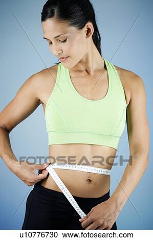 Stock Image - A young woman measuring her waist. Fotosearch