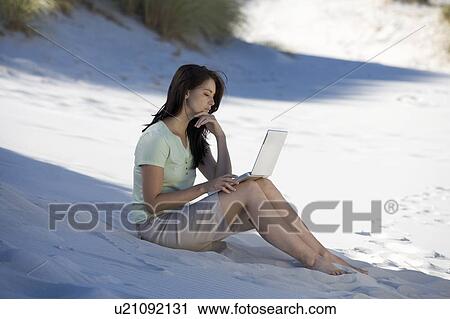 A young woman on a beach working on a laptop View Large Photo Image Stock Image - A young woman on a beach working on a laptop. Fotosearch