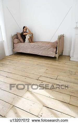 A young woman sitting on a bed View Large Photo Image Stock Image - A young woman sitting on a bed. Fotosearch