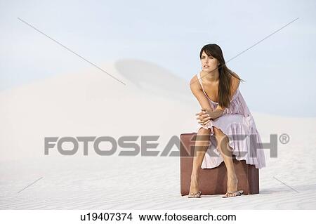 Picture - A young woman sitting on a suitcase in the desert. Fotosearch