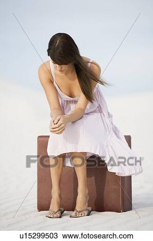 Stock Image - A young woman sitting on a suitcase in the desert. Fotosearch