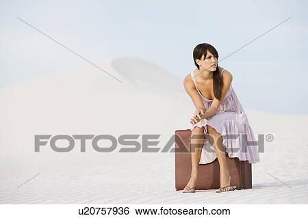 Stock Photograph - A young woman sitting on a suitcase in the desert. Fotosearch