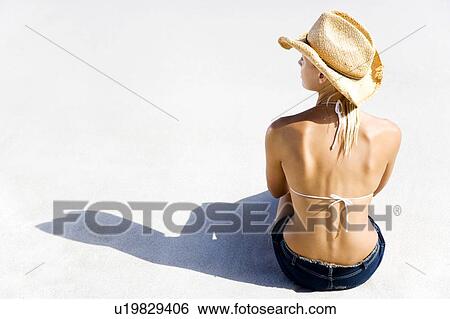 Stock Photograph - A young woman sitting on the beach. Fotosearch