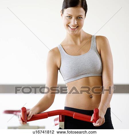 Stock Image - A young woman standing by an exercise bike. Fotosearch