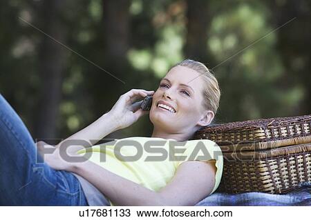 Stock Image - A young woman using a mobile phone at a picnic. Fotosearch