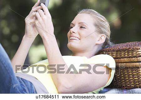 Stock Image - A young woman using a mobile phone at a picnic. Fotosearch