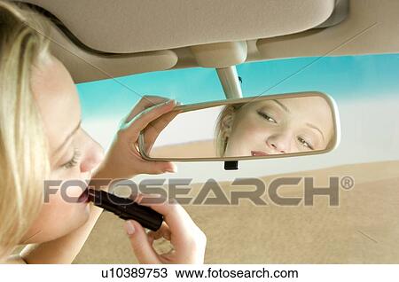 Stock Image - A young woman using a rear view mirror to apply make-up. Fotosearch