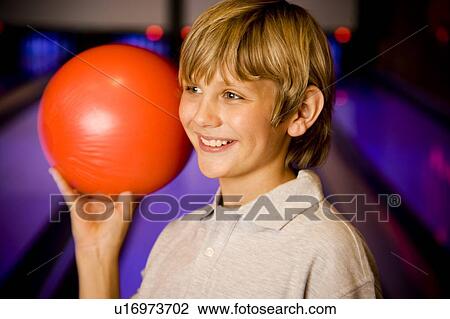 Stock Image - Boy in a bowling alley holding a red bowling ball. Fotosearch