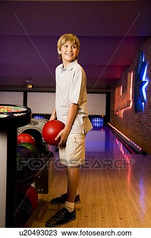 Stock Image - Boy in a bowling alley holding a red bowling ball. Fotosearch