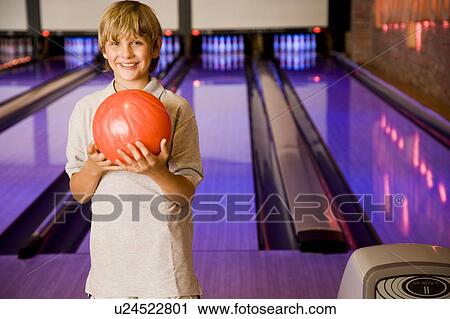 Stock Image - Boy in a bowling alley holding a red bowling ball. Fotosearch