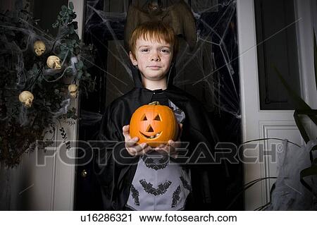 Stock Image - Boy in a skeleton costume at Hallowe'en, holding a pumpkin with a carved face. Fotosearch