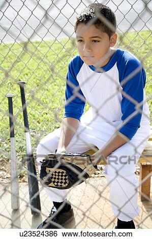 Stock Photograph - Boy in baseball gear sitting on a bench. Fotosearch