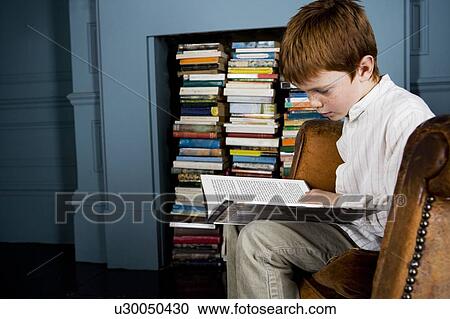 Stock Image - boy reading book sitting in armchair. Fotosearch