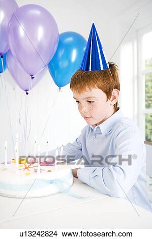 Boy sitting at table with birthday cake and balloons View Large Photo Image Picture - Boy sitting at table with birthday cake and balloons. Fotosearch