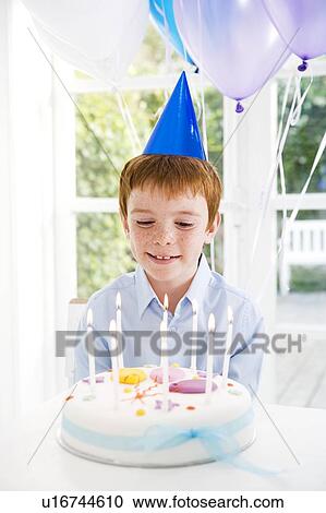 Stock Image - boy sitting at table with birthday cake. Fotosearch