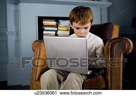 Stock Image - boy sitting in armchair using laptop computer. Fotosearch