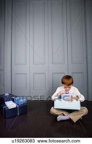 Stock Image - boy sitting on the floor looking at his presents. Fotosearch