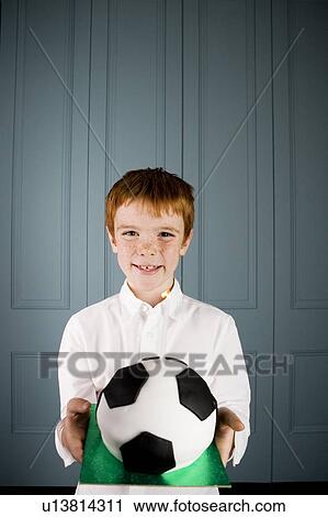 Stock Image - boy with ginger hair holding football birthday cake. Fotosearch