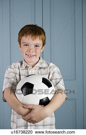 Stock Image - boy with ginger hair smiling and holding football. Fotosearch