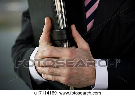 Stock Photo - Businessman holding a leather case with briefing papers, close up of hands. Fotosearch